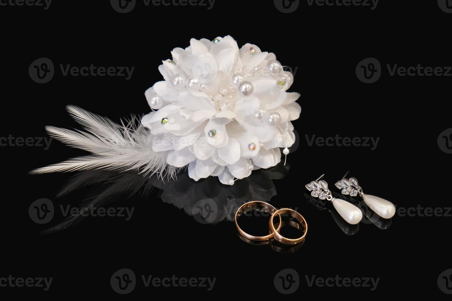 deux mariage anneaux, des boucles d'oreilles de le la mariée et du marié boutonnière sur noir Contexte avec réflexion. mariage symboles photo