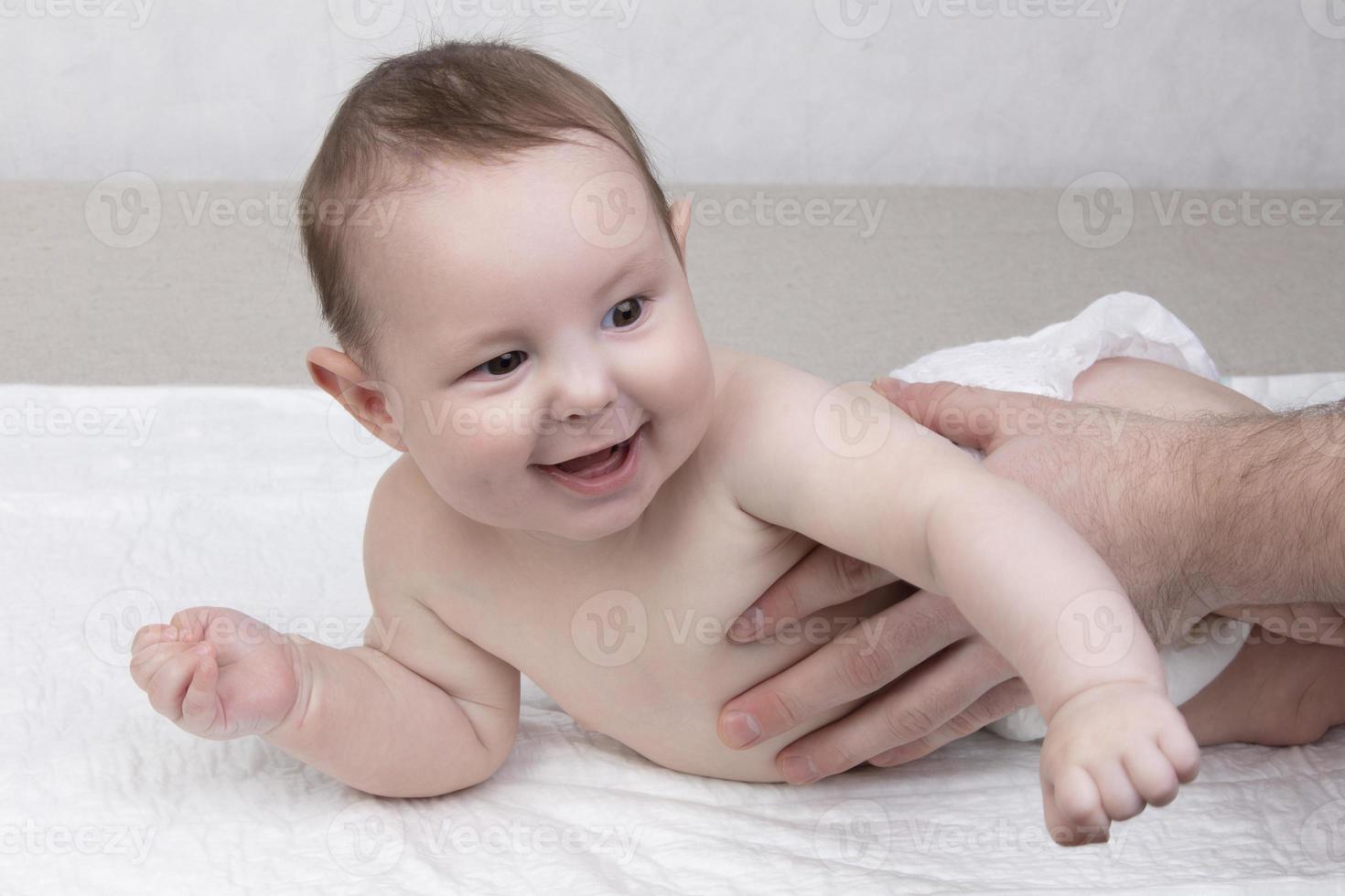 une six mois garçon dans une couche mensonges sur une couche, le sien du père main les soutiens lui photo