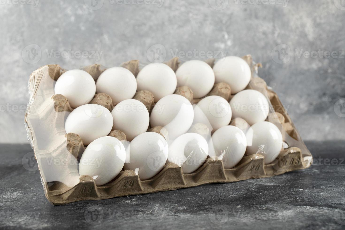 Œufs de poule crus dans une boîte à œufs sur un fond de marbre photo