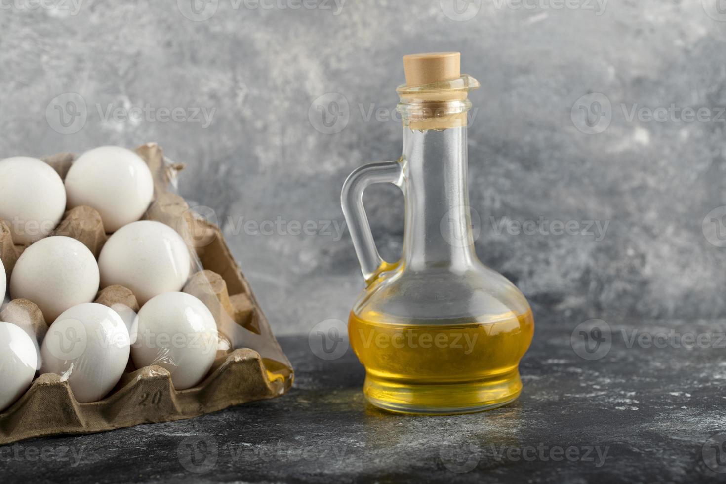 œufs de poule crus dans une boîte à œufs avec une bouteille en verre d'huile photo