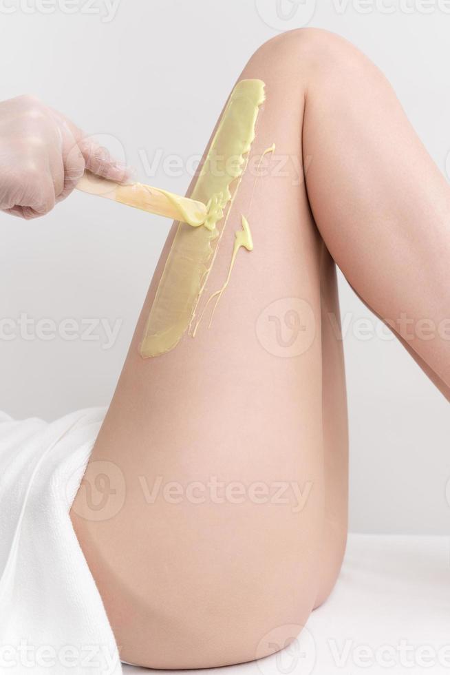 main dans gant appliquant vert chaud la cire sur svelte femme jambe en utilisant spatule. épilation procédure photo