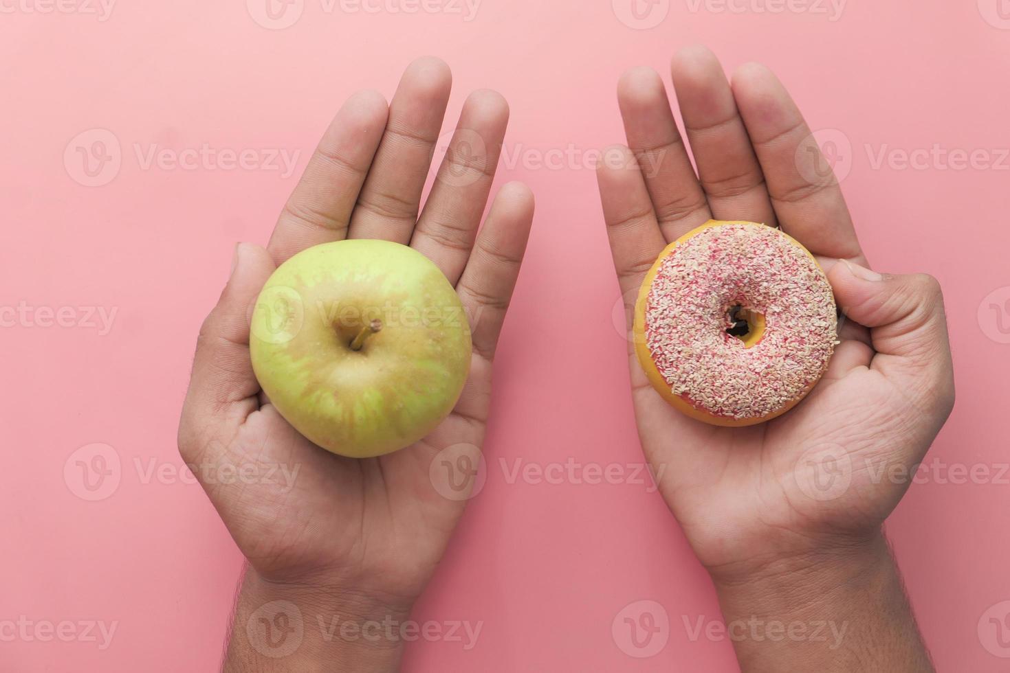 tenant une pomme verte et petit beignet sur fond rose photo