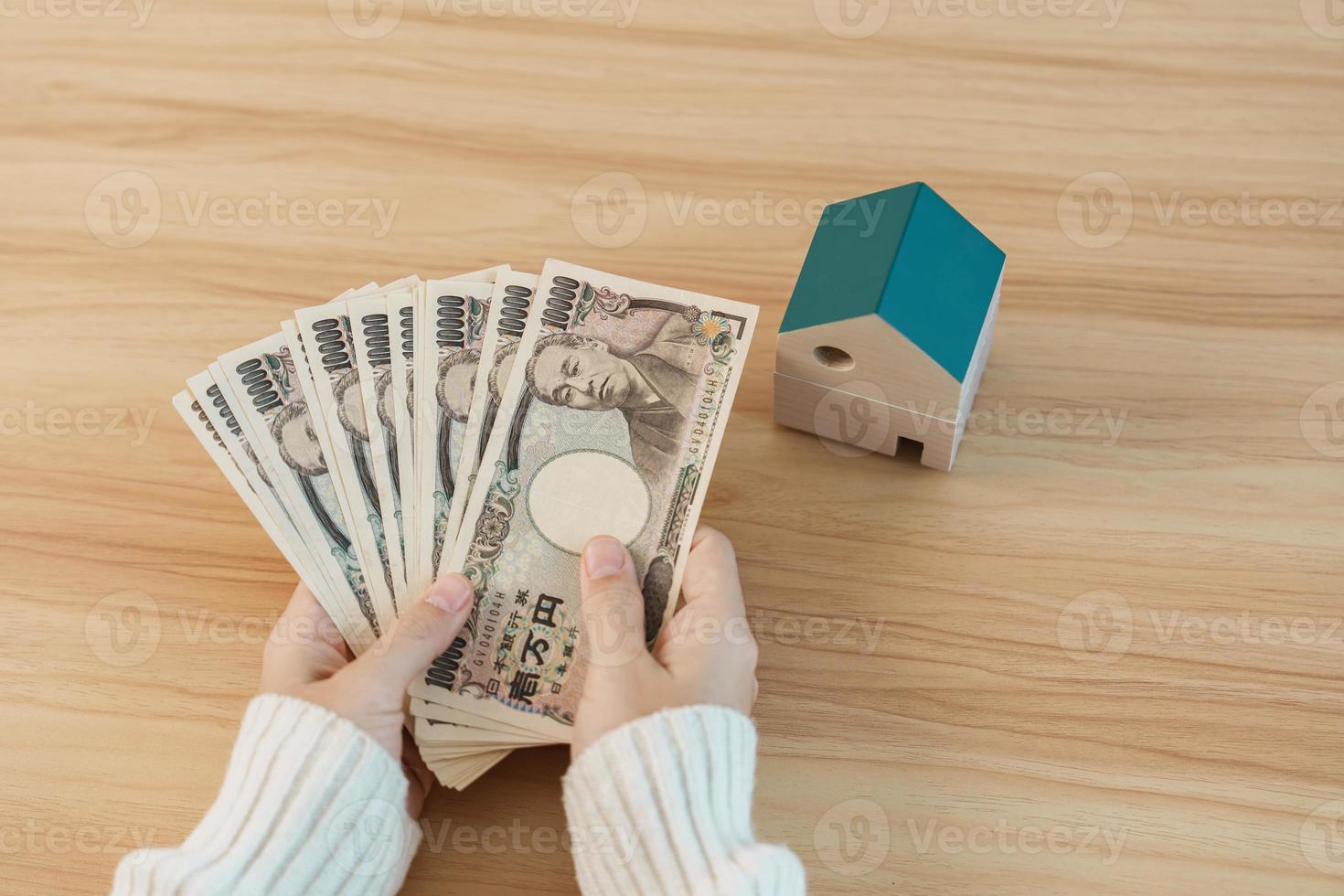 femme tenant un billet de yen japonais et un modèle de maison. immobilier, maison, hypothèque, trésorerie japonaise, impôt, économie de récession, inflation, investissement, finances et concepts d'épargne photo