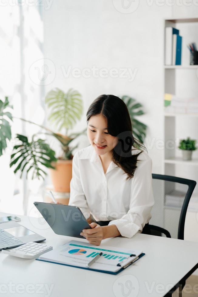 belle jeune femme utilisant un ordinateur portable et une tablette tout en étant assise sur son lieu de travail. concentré au travail. photo