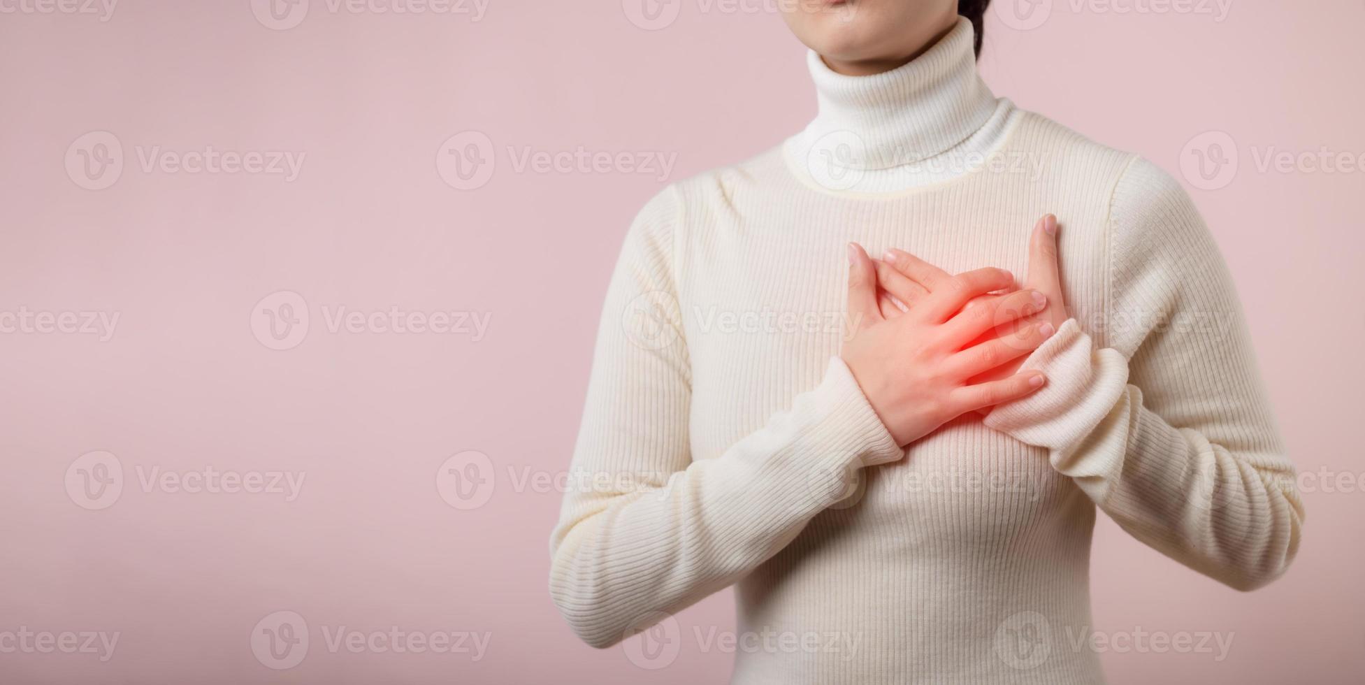 Jeune femme Souffrance de cœur attaque sur lumière rose studio Contexte. douloureux crampes, cœur maladie, pressage sur poitrine avec douloureux expression. soins de santé monde santé journée concept. photo