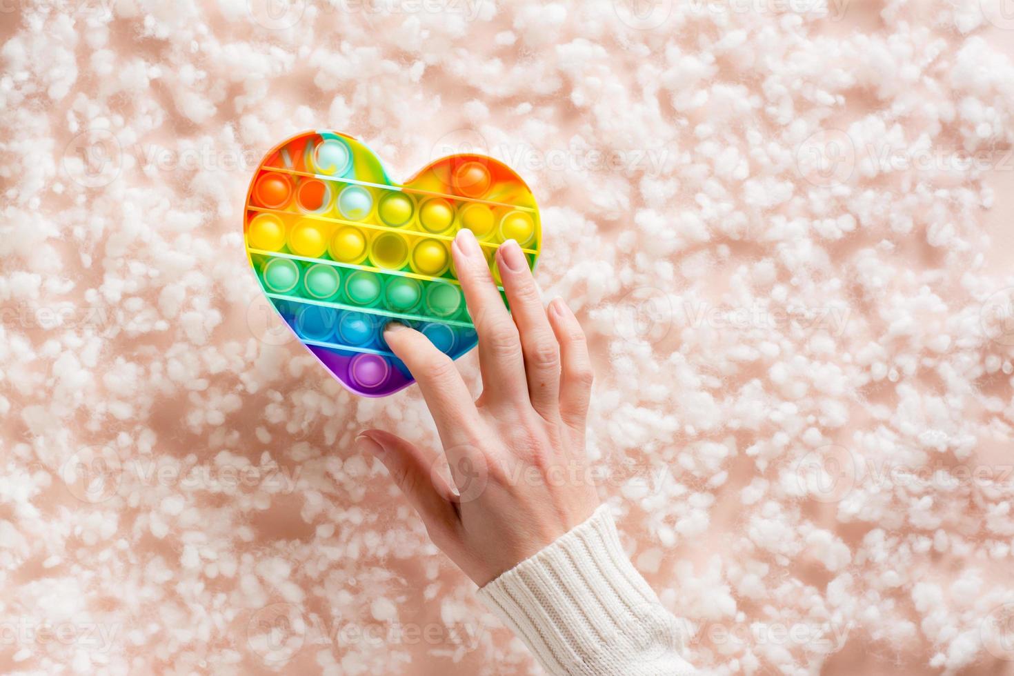 une femelle main presses une silicone arc en ciel anti stress jouet sur une Contexte de duvet. une moderne façon à se détendre photo