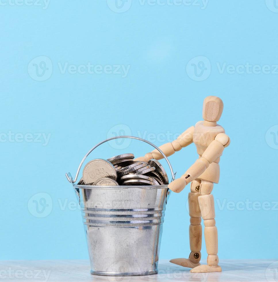 une en bois mannequin et pièces de monnaie dans une miniature seau sur une bleu arrière-plan, une concept de haute revenu, subvention photo