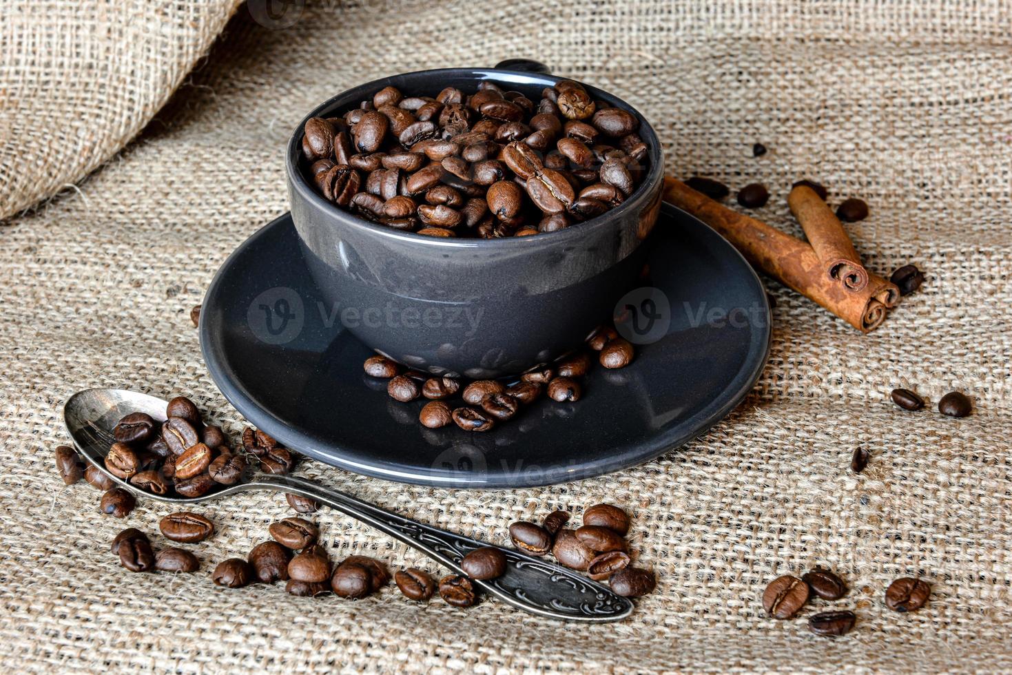 Tasse à café noire pleine de grains de café bio et de bâtons de cannelle sur un chiffon en lin photo