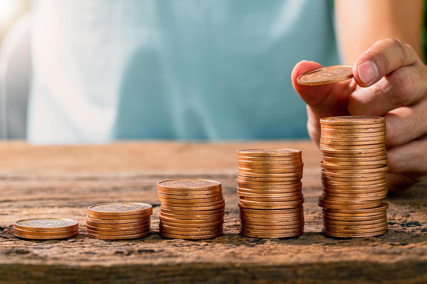 Une personne tenant une pièce avec une pile de pièces sur une table en bois, concept d'investissement photo