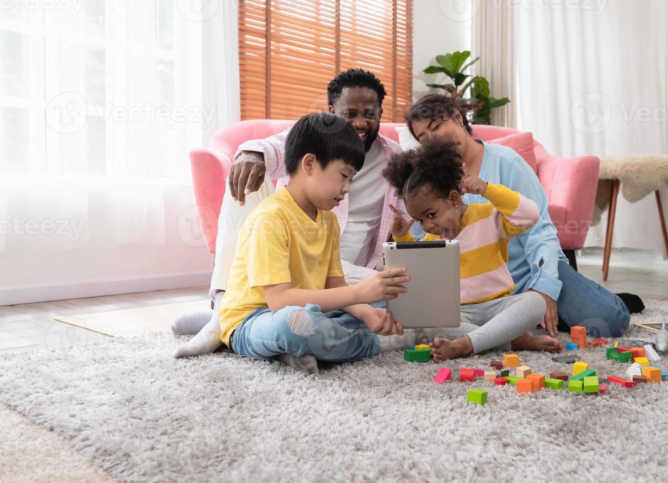 souriant famille et marrant fille sur vidéo appel à maison. quatre gens séance sur tapis dans vivant pièce photo
