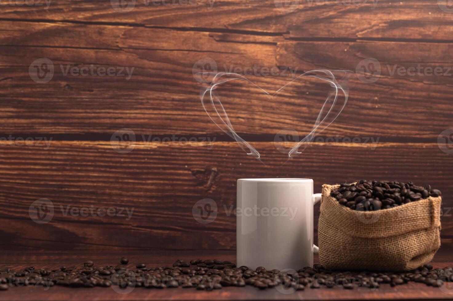 Une tasse de café faisant de la vapeur en forme de coeur avec un sac de grains de café sur une table en bois photo