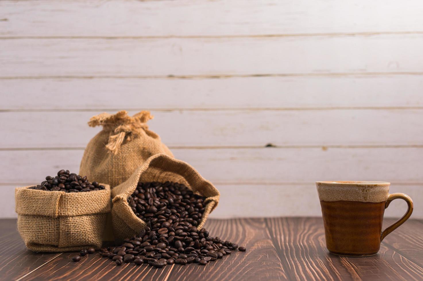 Une tasse de café et des sacs de grains de café sur une table en bois photo