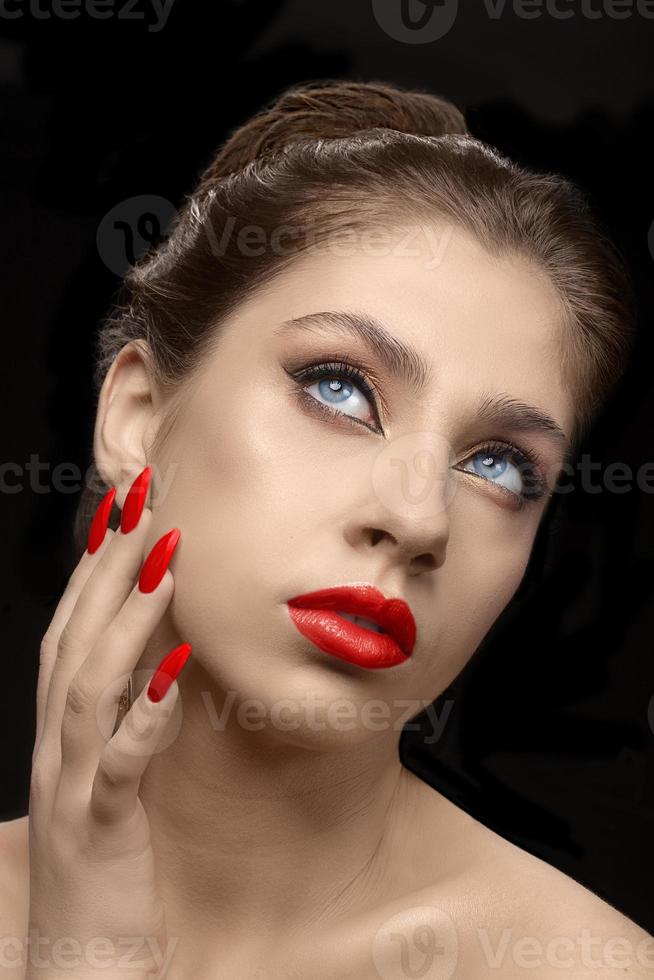 modèle avec rouge rouge à lèvres et magnifique manucure sur une foncé Contexte. le visage de une magnifique bien soigné brunette fille avec nettoyer peau. photo