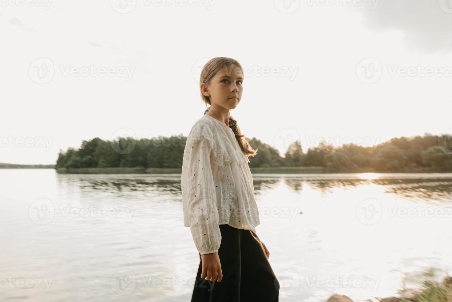 Un portrait flou d'une jeune fille qui marche sur la côte du lac au coucher du soleil photo