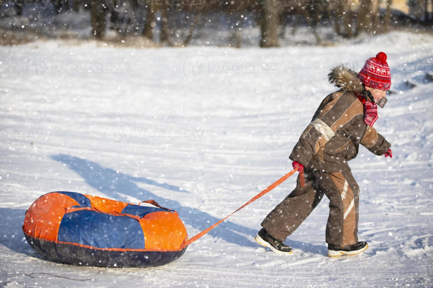 peu enfant sur une traîneau. enfant sur une hiver journée. une garçon est équitation sur une neige glisser. tirer le traîneau. photo