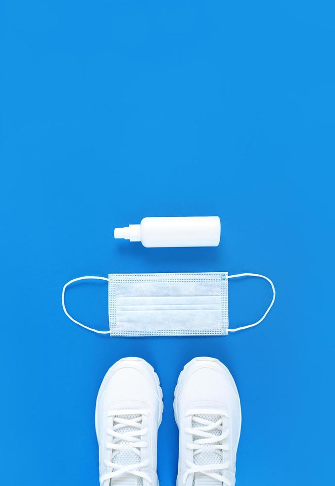 Masque médical blanc, formateurs et désinfectant pour les mains sur fond bleu, mise à plat verticale monochrome photo
