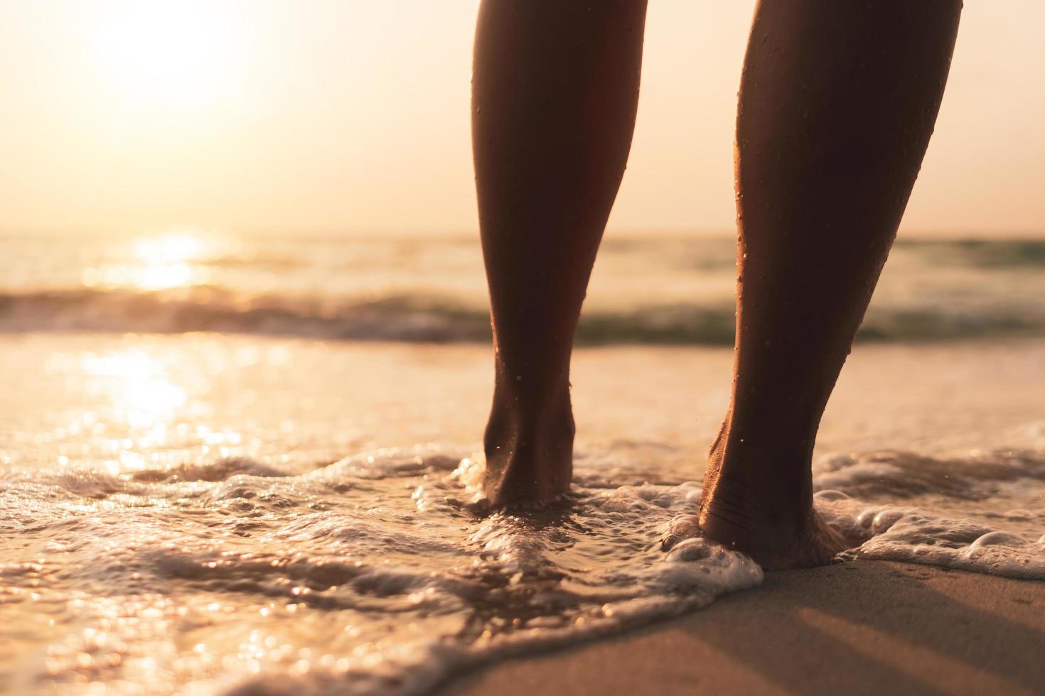 les pieds d'une femme dans l'eau à la plage au coucher du soleil photo