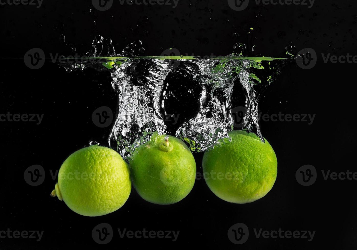 Frais vert citrons verts laissez tomber dans le l'eau photo