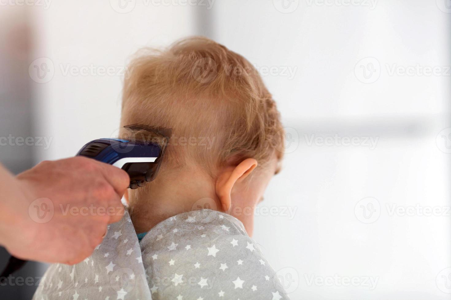 femelle mains Couper une enfant avec une cheveux tondeuse dans une coiffeur. le premier la Coupe de cheveux. photo