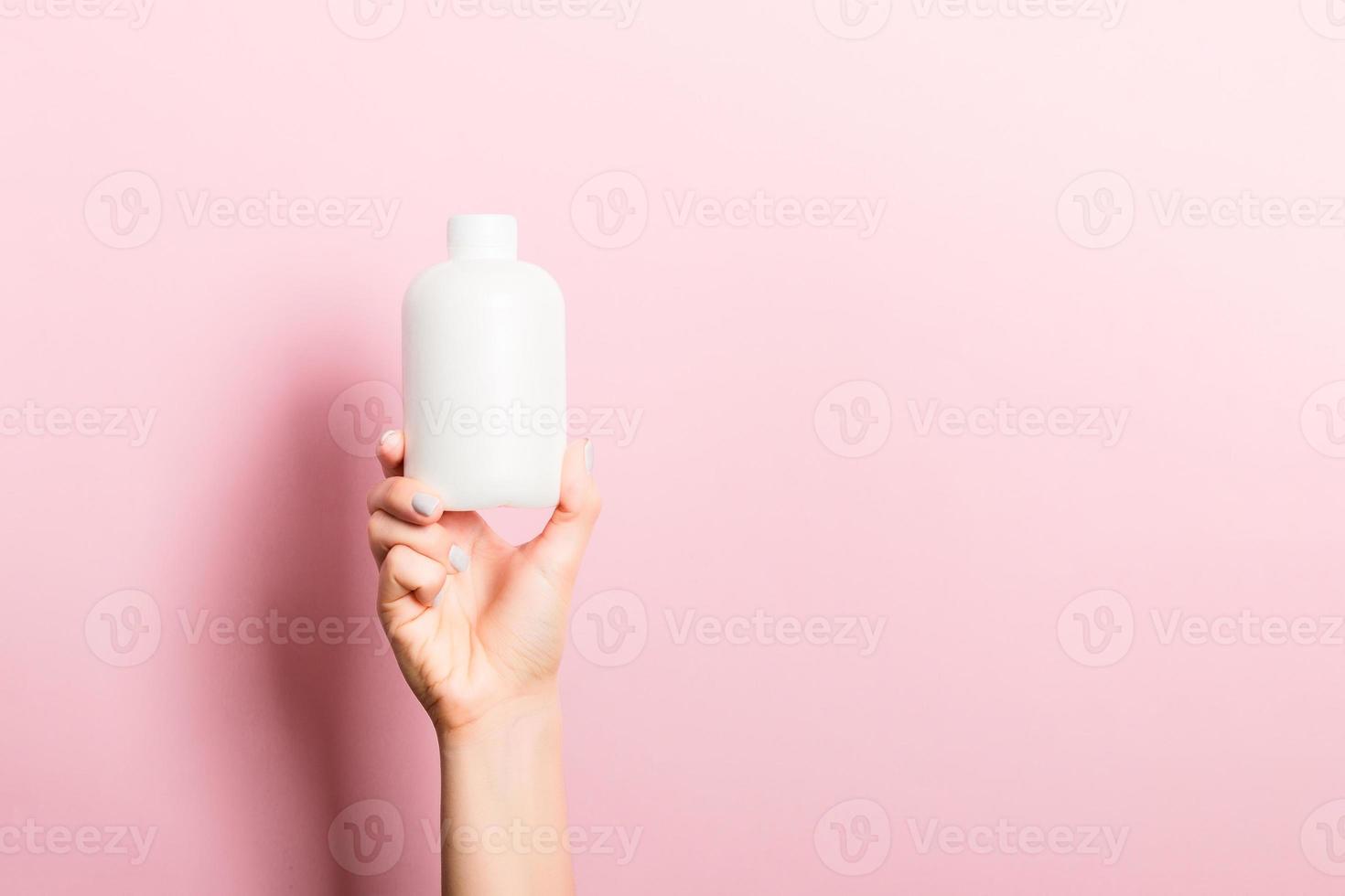 femelle main en portant crème bouteille de lotion isolé. fille donner tube cosmétique des produits sur rose Contexte photo