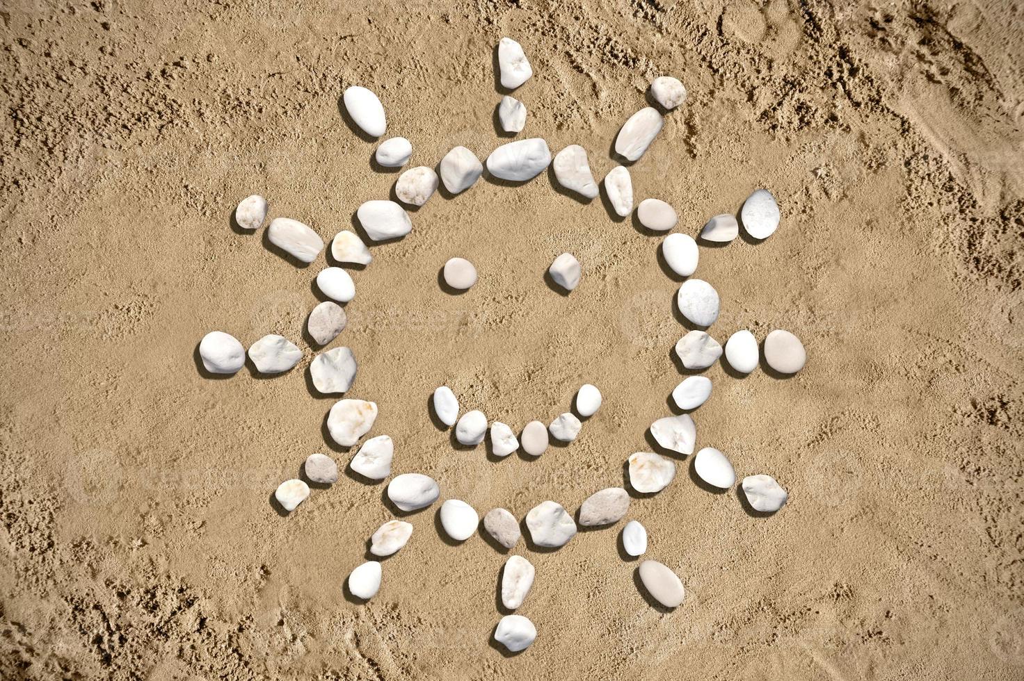 Soleil avec une sourire fabriqué avec des pierres sur le sable photo