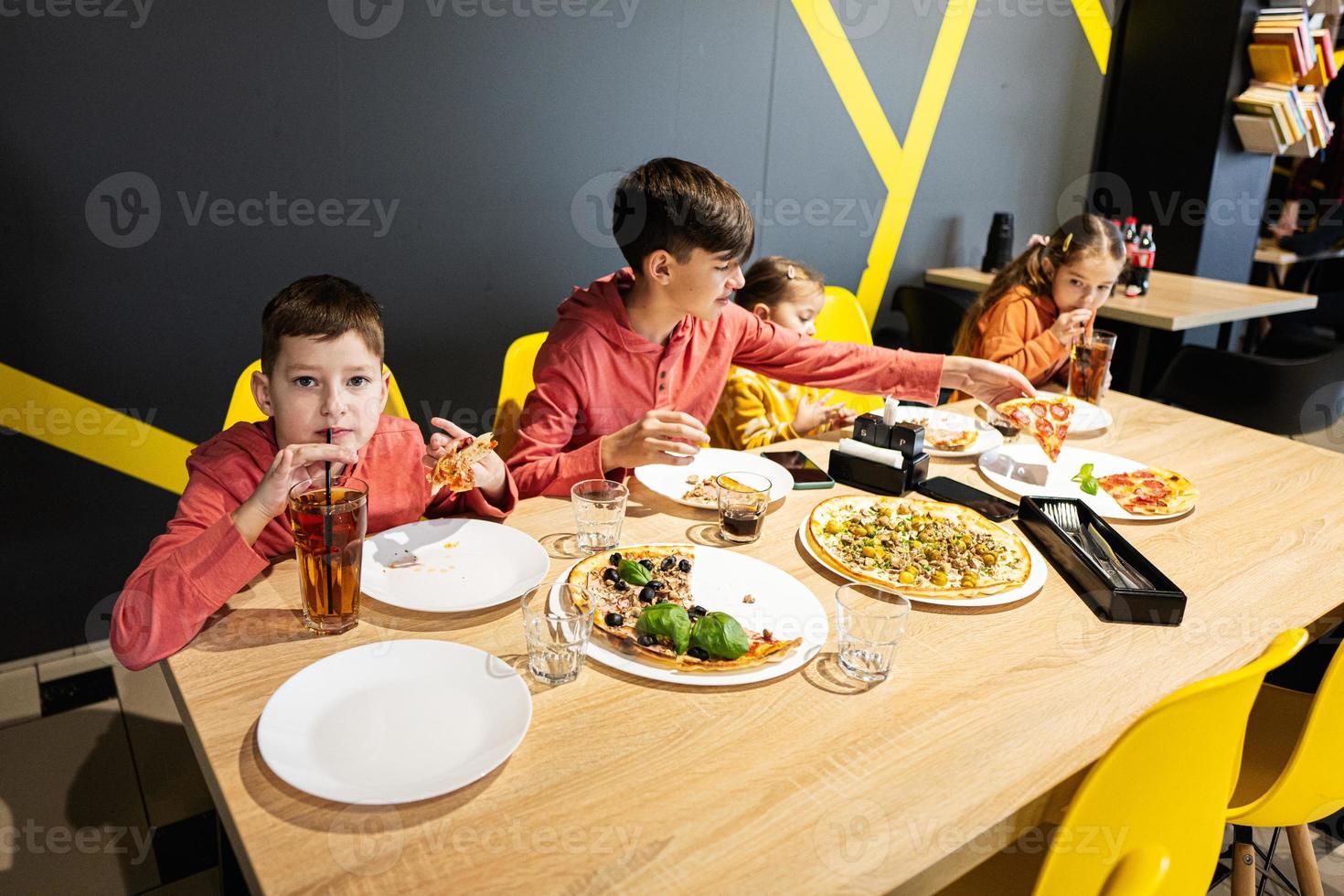 quatre des gamins en mangeant italien Pizza dans pizzeria. les enfants manger à café. garçon boisson jus. photo