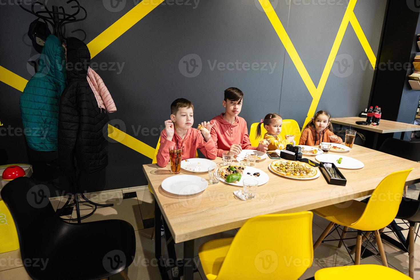 quatre des gamins en mangeant italien Pizza dans pizzeria. les enfants manger à café. photo