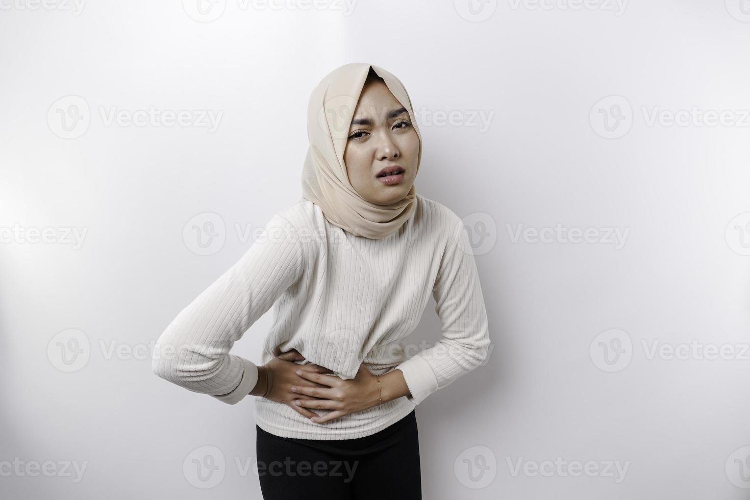 un asiatique musulman femme est jeûne et faim et émouvant sa ventre tandis que à la recherche de côté en pensant à propos quoi à manger photo