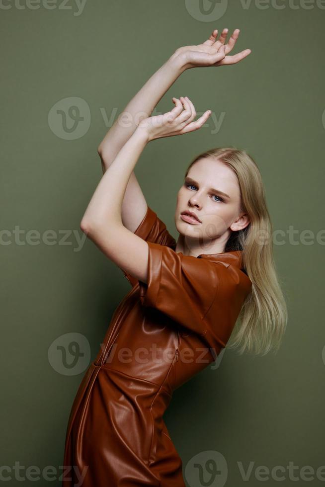 professionnel blond Jeune femelle modèle dans marron branché robe en portant mains en haut sérieux regards à caméra courbure dansant posant isolé sur plus de olive vert studio mur Contexte. saisonnier vente bannière photo