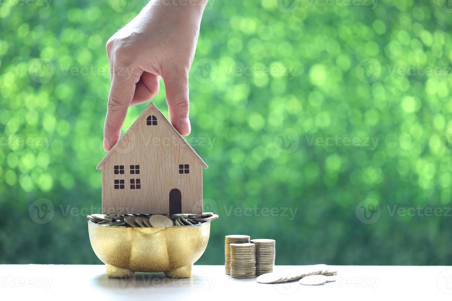 Pile de pièces en bois tirelire et maison modèle sur fond vert naturel photo