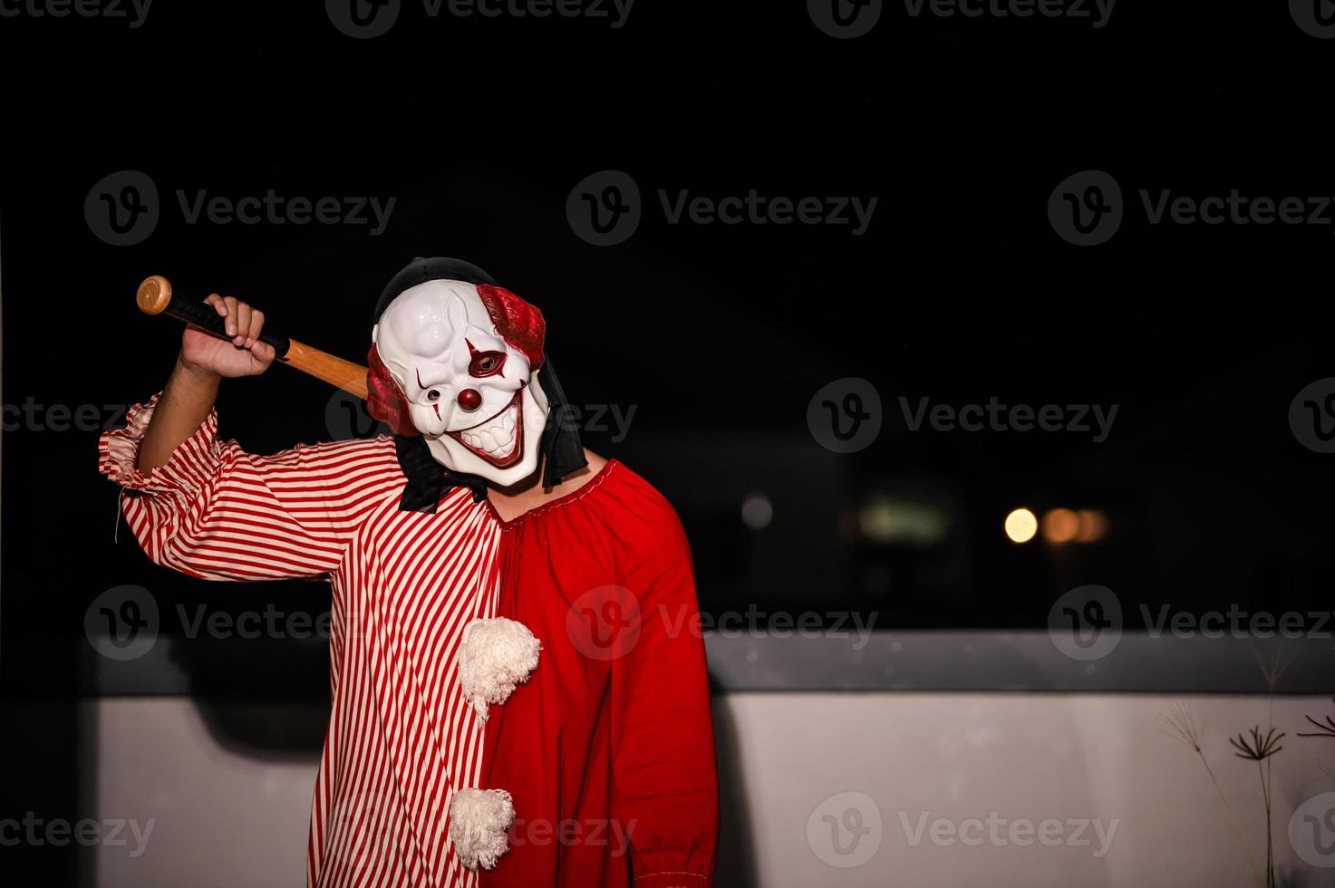 asiatique Beau homme porter pitre masque avec arme à le nuit scène, halloween Festival concept, horreur effrayant photo de une tueur dans Orange tissu, mal pitre caractère