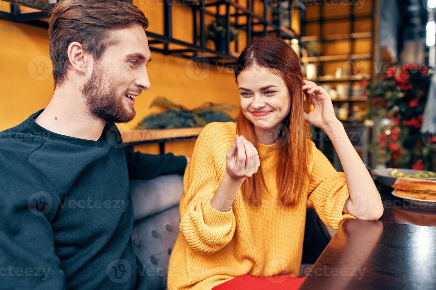 Beau homme et content femme dans chandail sont séance à une table dans une café bavardage pièce intérieur photo