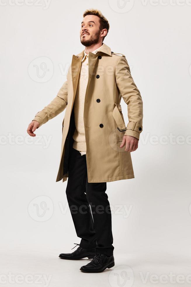 une homme dans une beige manteau et pantalon sur une lumière Contexte bottes copie espace photo