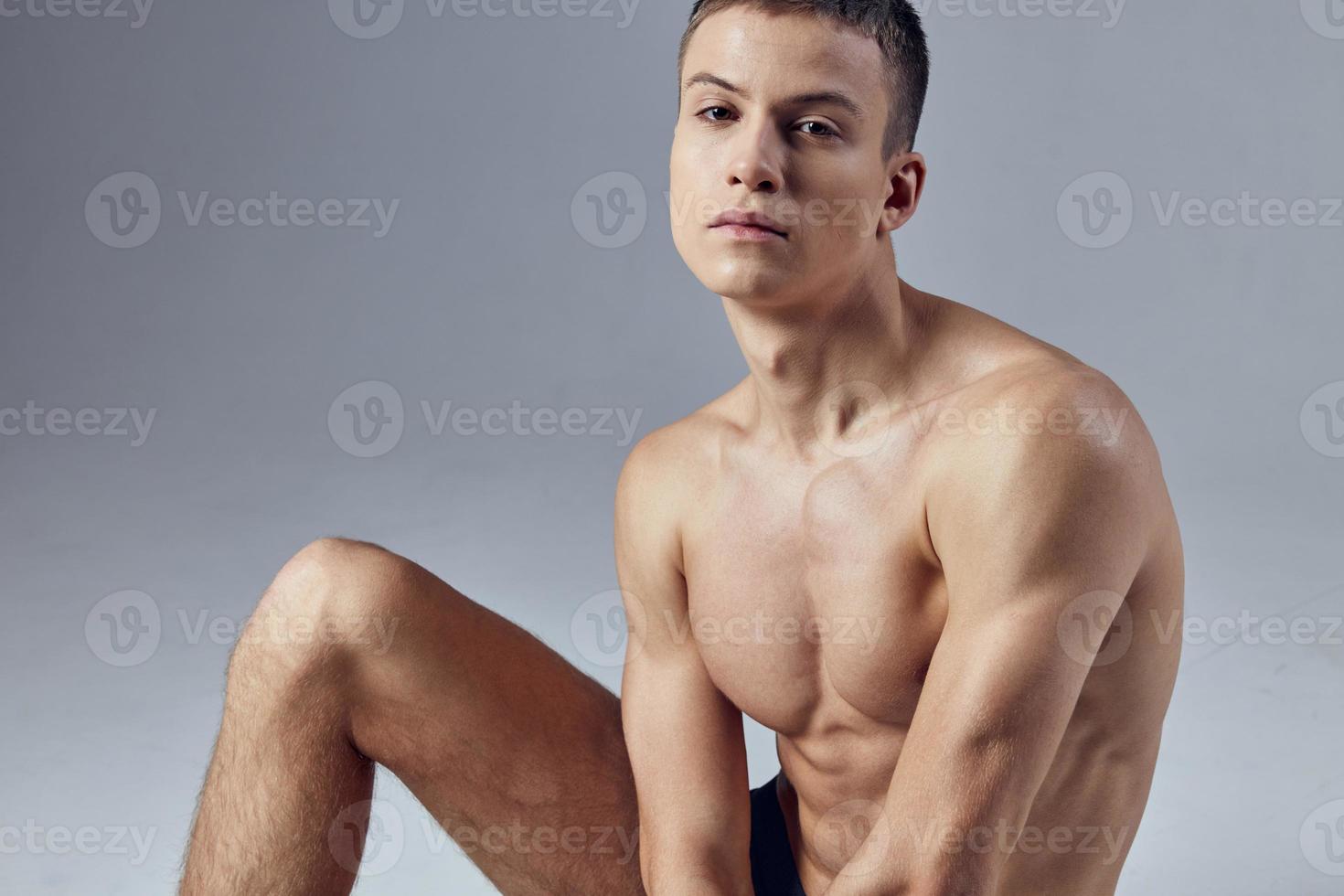 sportif homme avec une gonflé à bloc corps dans noir short est assis sur le sol photo