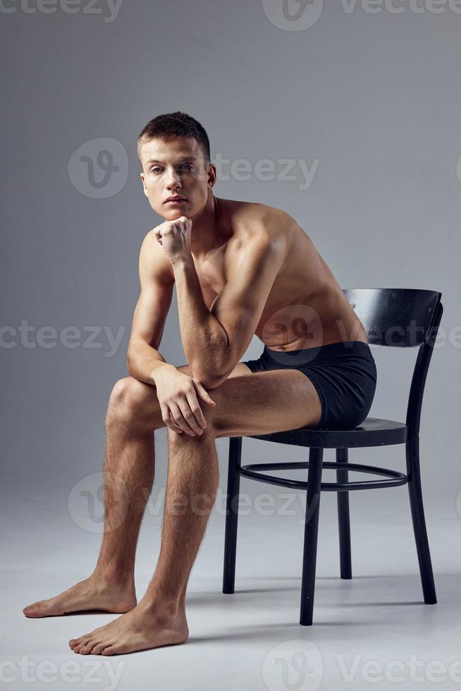 sportif homme avec une pompé en haut corps dans noir short est assis sur une chaise photo