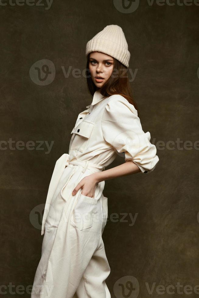 à la mode femme dans une chaud chapeau et dans une blanc combinaison détient sa mains sur sa ceinture photo