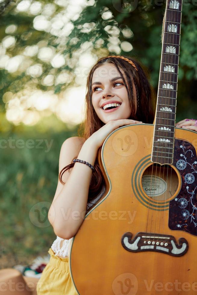 Jeune hippie femme avec éco image souriant et à la recherche dans le caméra avec guitare dans main dans la nature sur une voyage photo