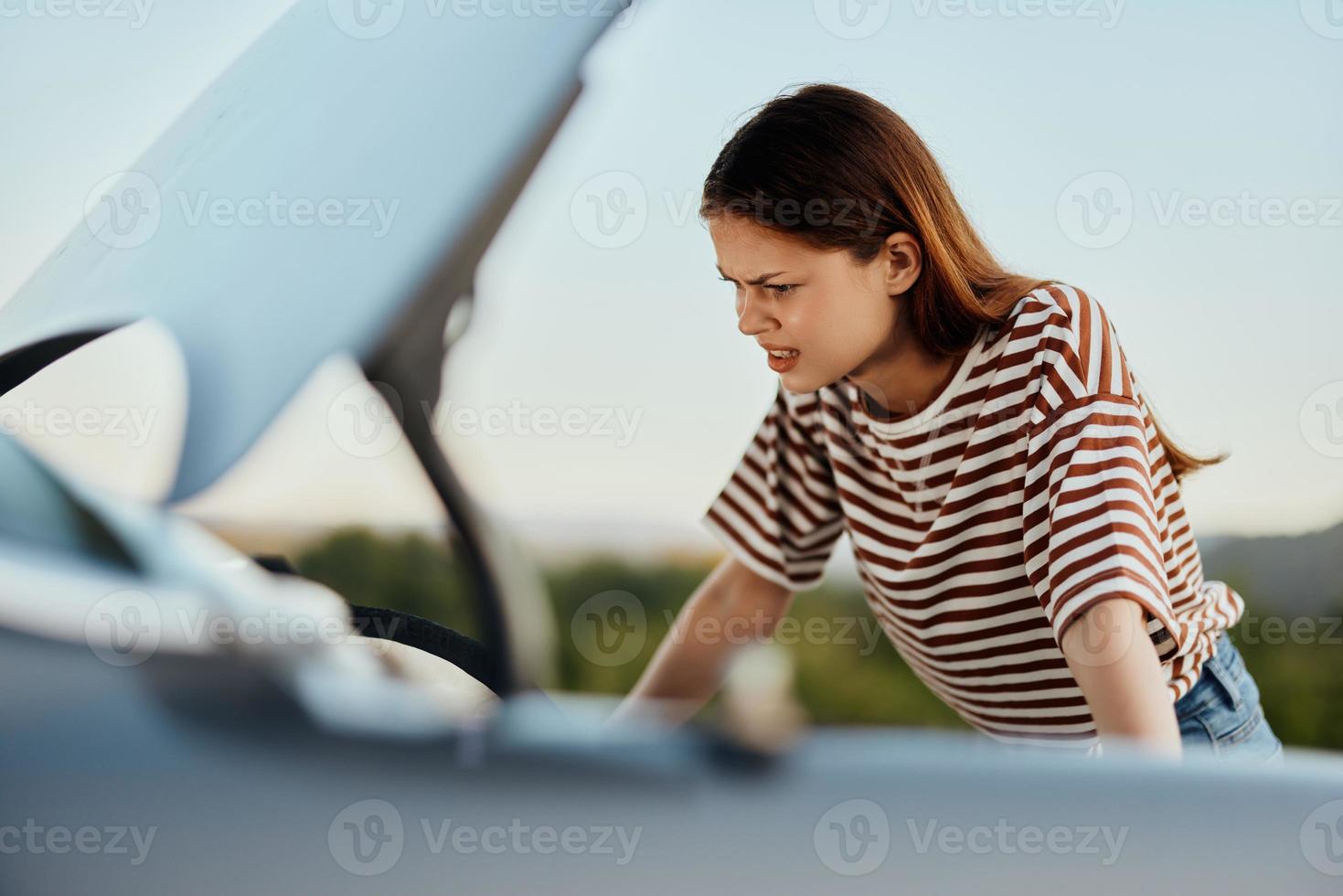 une triste femme regards dans incrédulité à sa cassé vers le bas voiture sur le route tandis que en voyageant et Est-ce que ne pas connaître quoi à faire photo