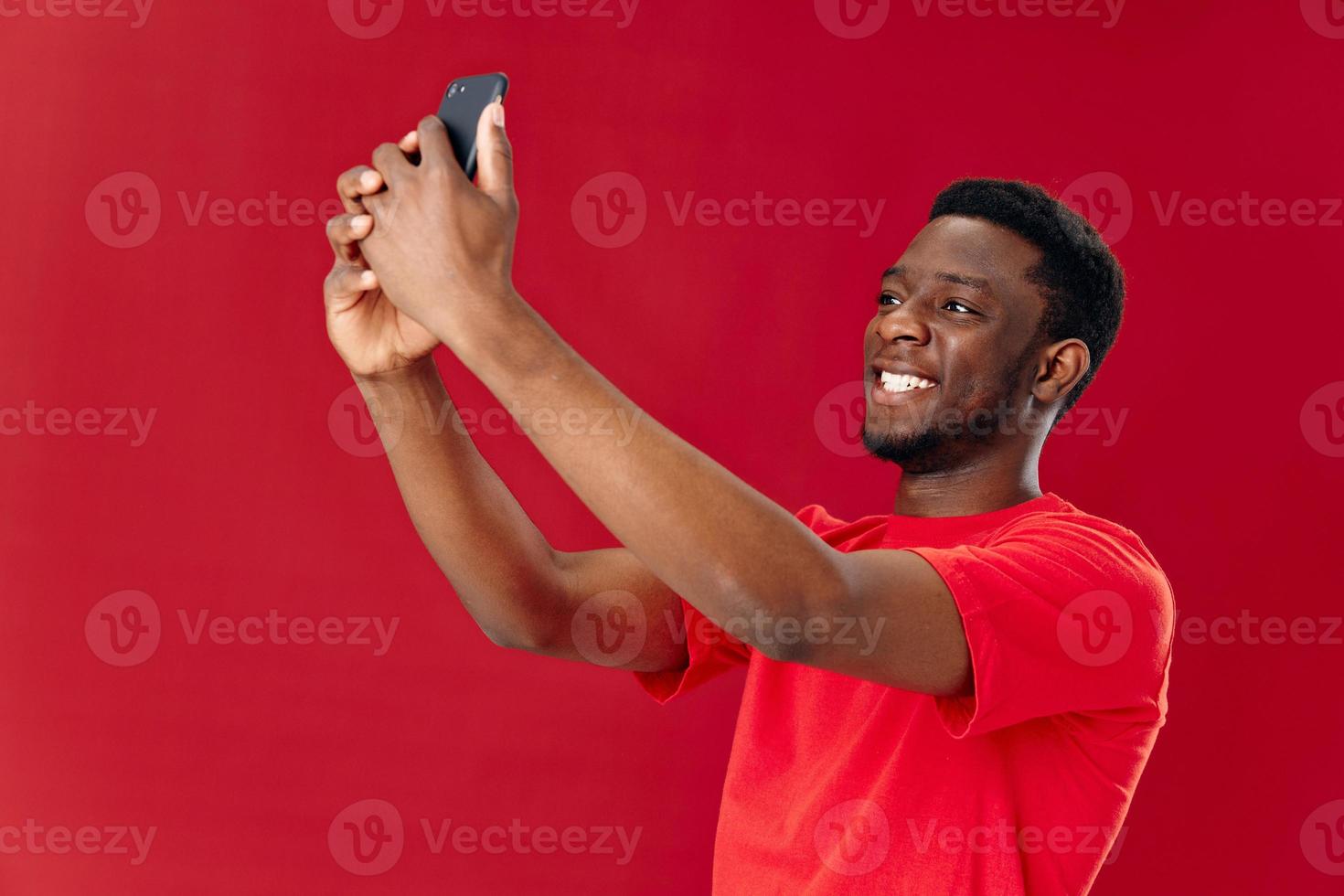 de bonne humeur homme de africain apparence avec téléphone dans mains tondu vue isolé La technologie Contexte photo