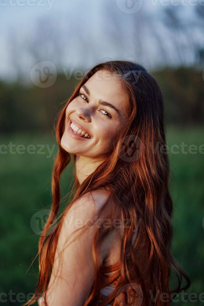 portrait de une femme avec une magnifique sourire dans été vert la nature contre le herbe, à la recherche en dehors à le réglage Soleil. le concept de santé et beauté photo