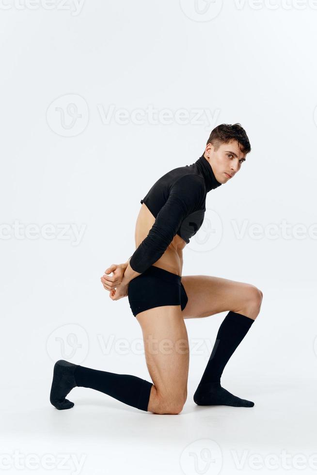 une homme avec un athlétique physique des stands sur le sien le genou dans une chandail caleçon et chaussettes sur une lumière Contexte côté vue photo