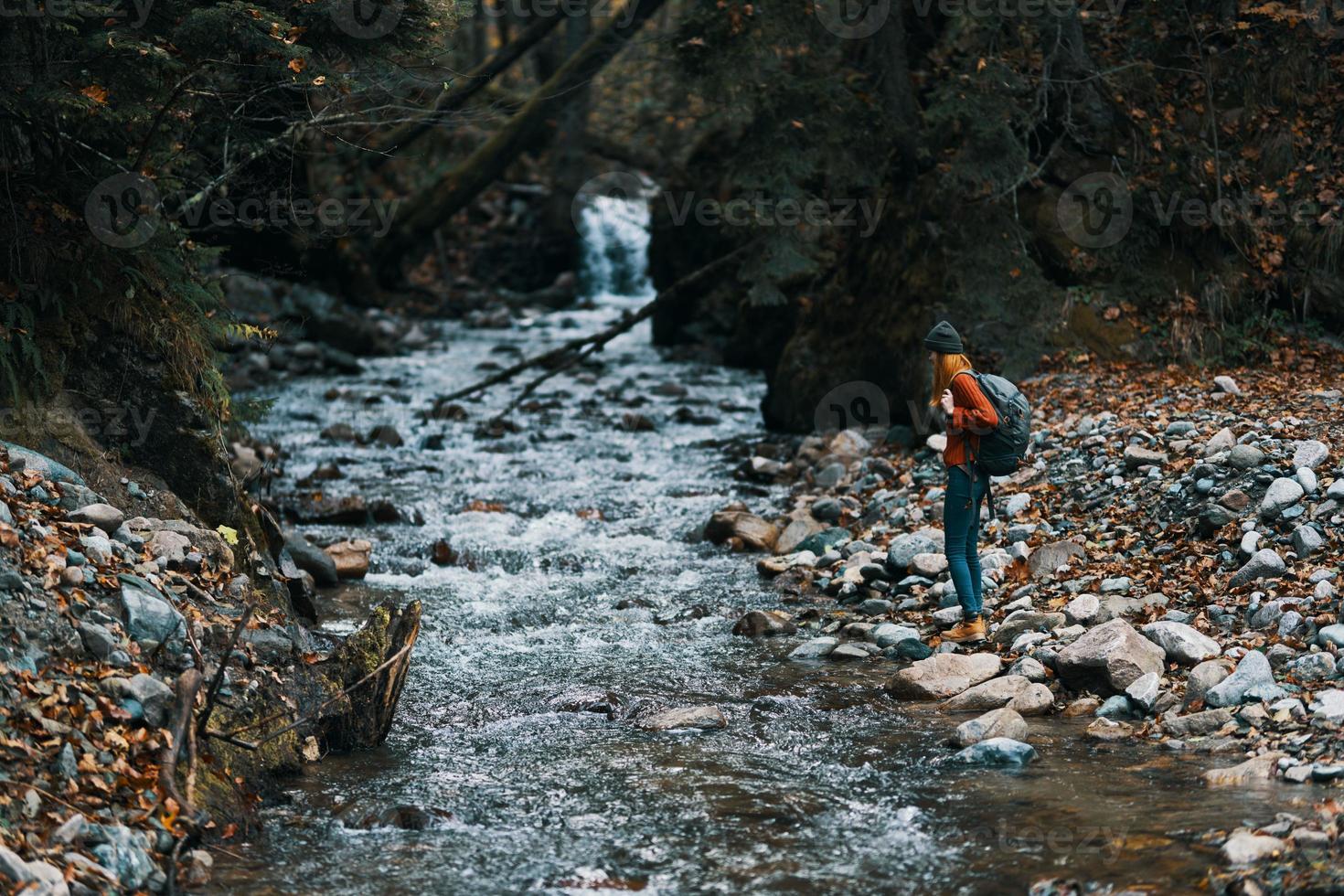 femme dans le montagnes près le rivière avec une sac à dos sur sa retour et une forêt dans le Contexte photo