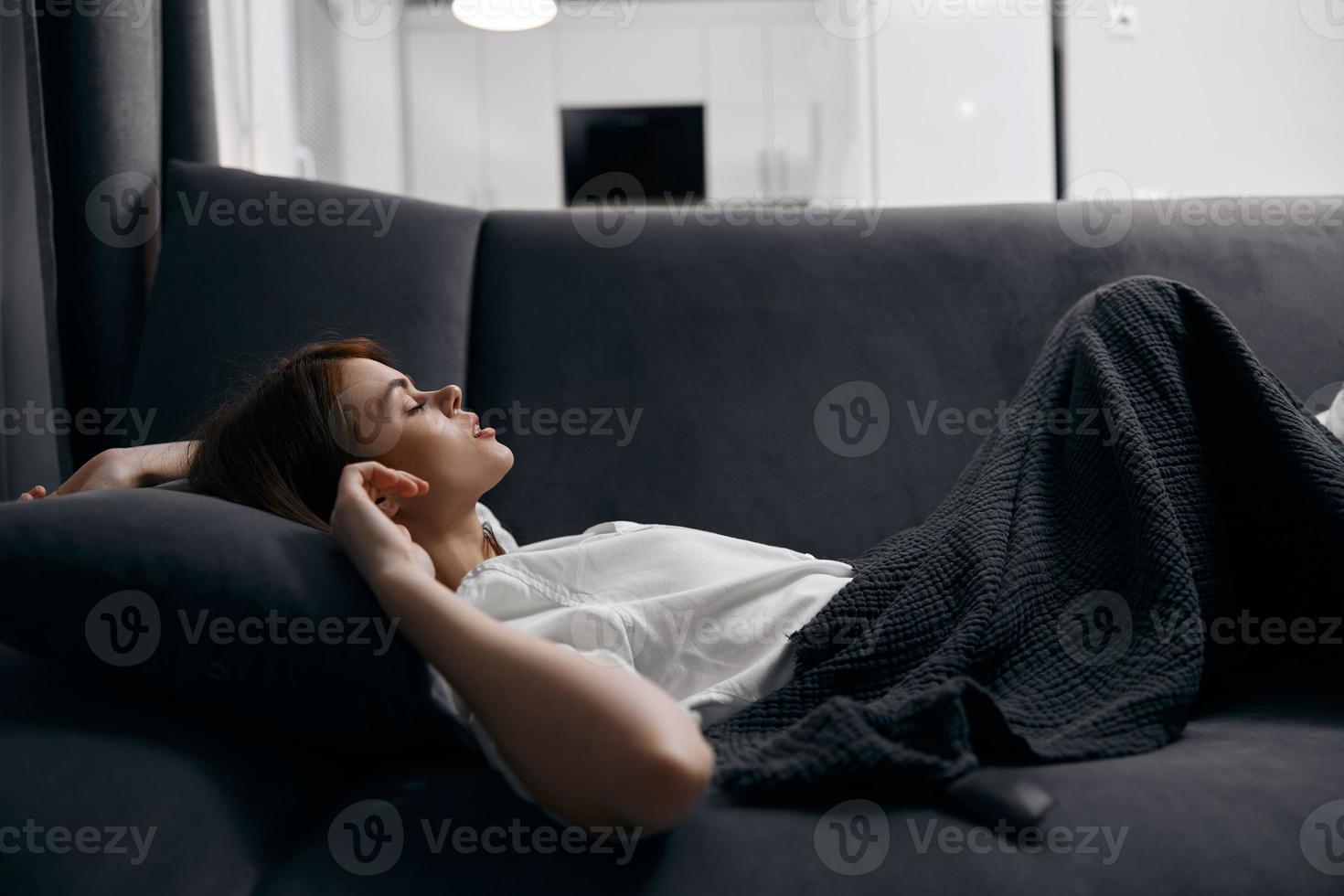 femme repos mensonge sur une canapé en dessous de une gris couverture photo