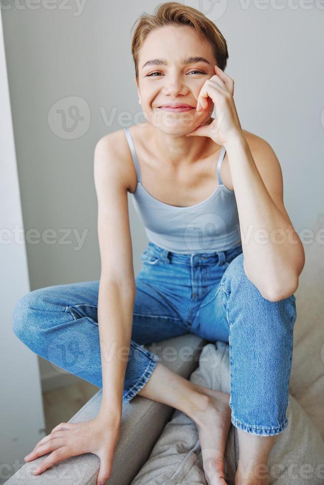 Jeune femme avec court la Coupe de cheveux cheveux ayant amusement à Accueil sur le canapé sourire et bonheur, vacances à maison, Naturel posant sans pour autant filtres, gratuit copie espace photo