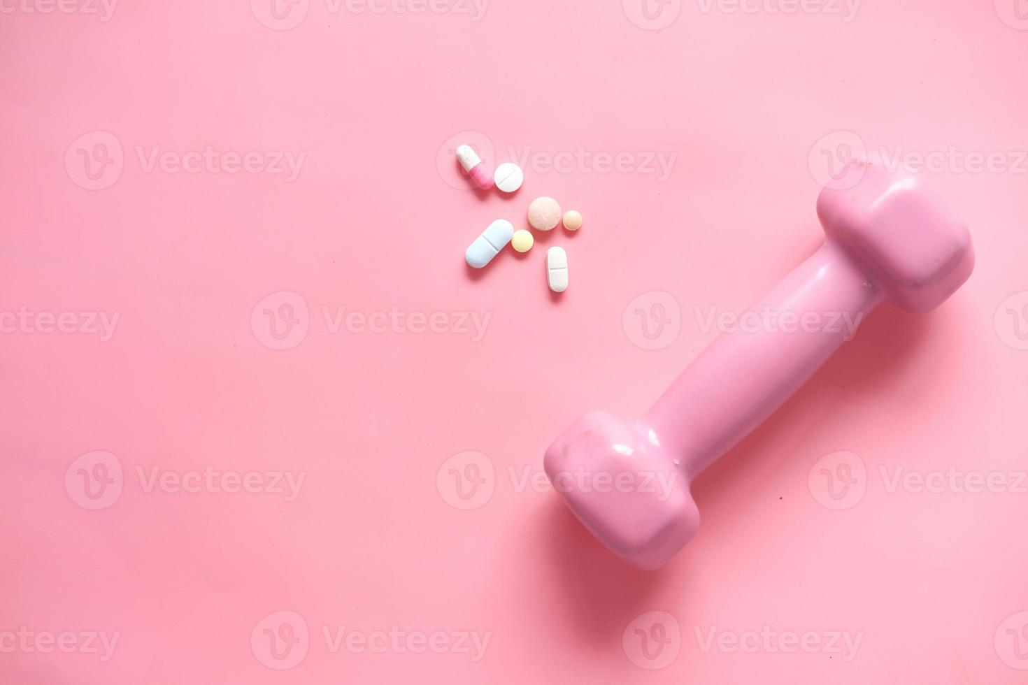 Haltère de couleur rose et pilules médicales sur fond rose photo