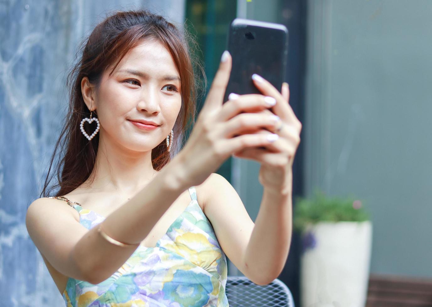 Belle femme asiatique utilisant joyeusement un smartphone pour prendre des selfies à la maison photo