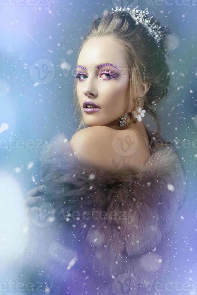 le neige reine. hiver fille dans une fourrure manteau douché avec neige. modèle avec magnifique maquillage sur une neigeux Contexte. photo