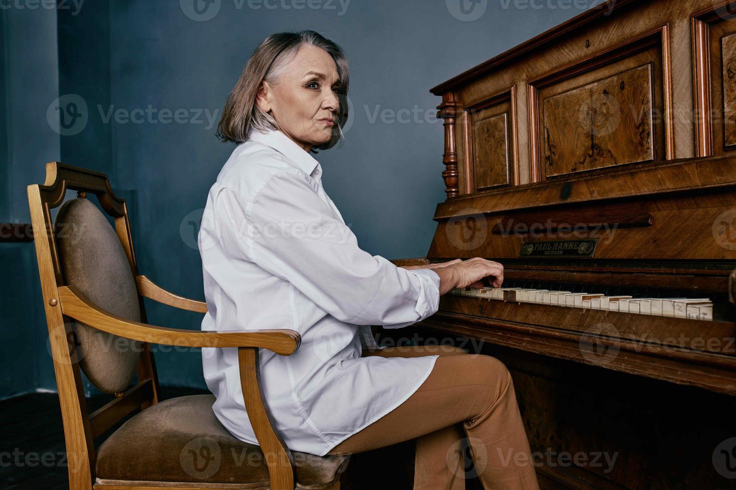 une femme dans une blanc chemise est assis sur une chaise suivant à une piano apprentissage la musique photo