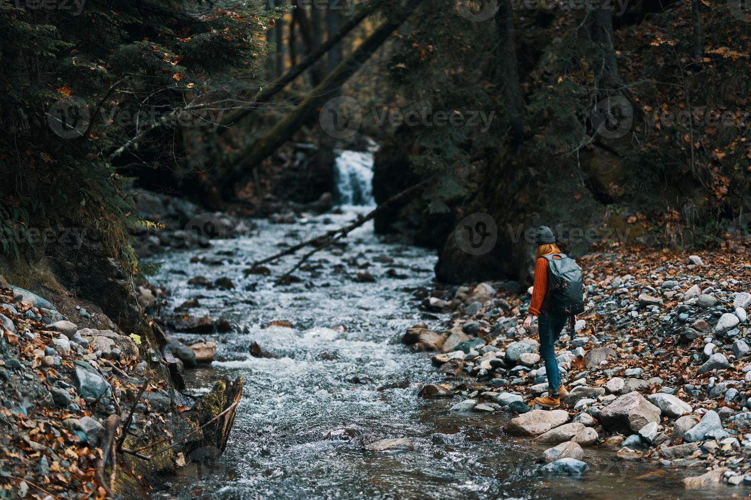 femme dans le montagnes près le rivière avec une sac à dos sur sa retour et une forêt dans le Contexte photo