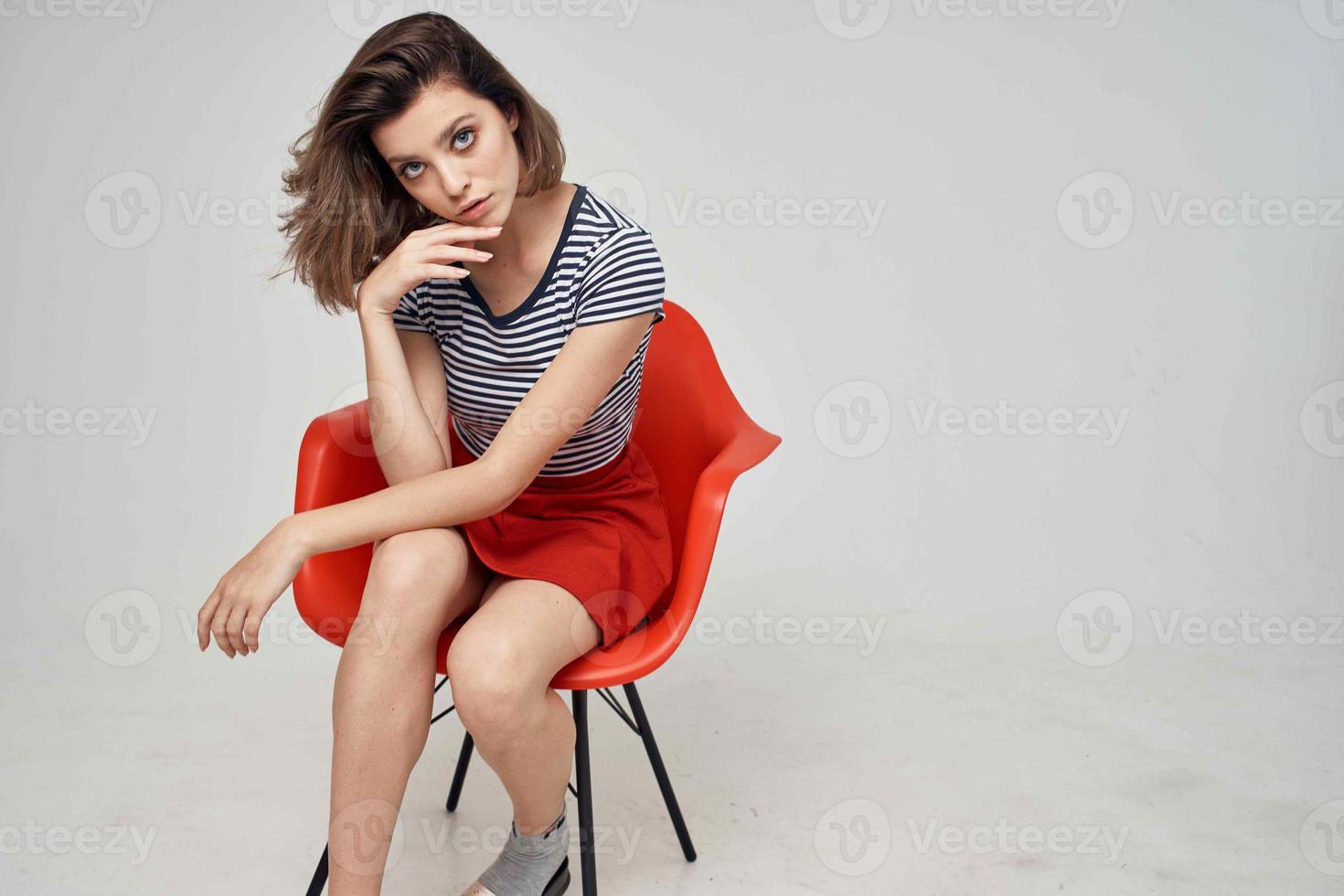 jolie femme dans à la mode vêtements séance sur le rouge chaise posant studio photo